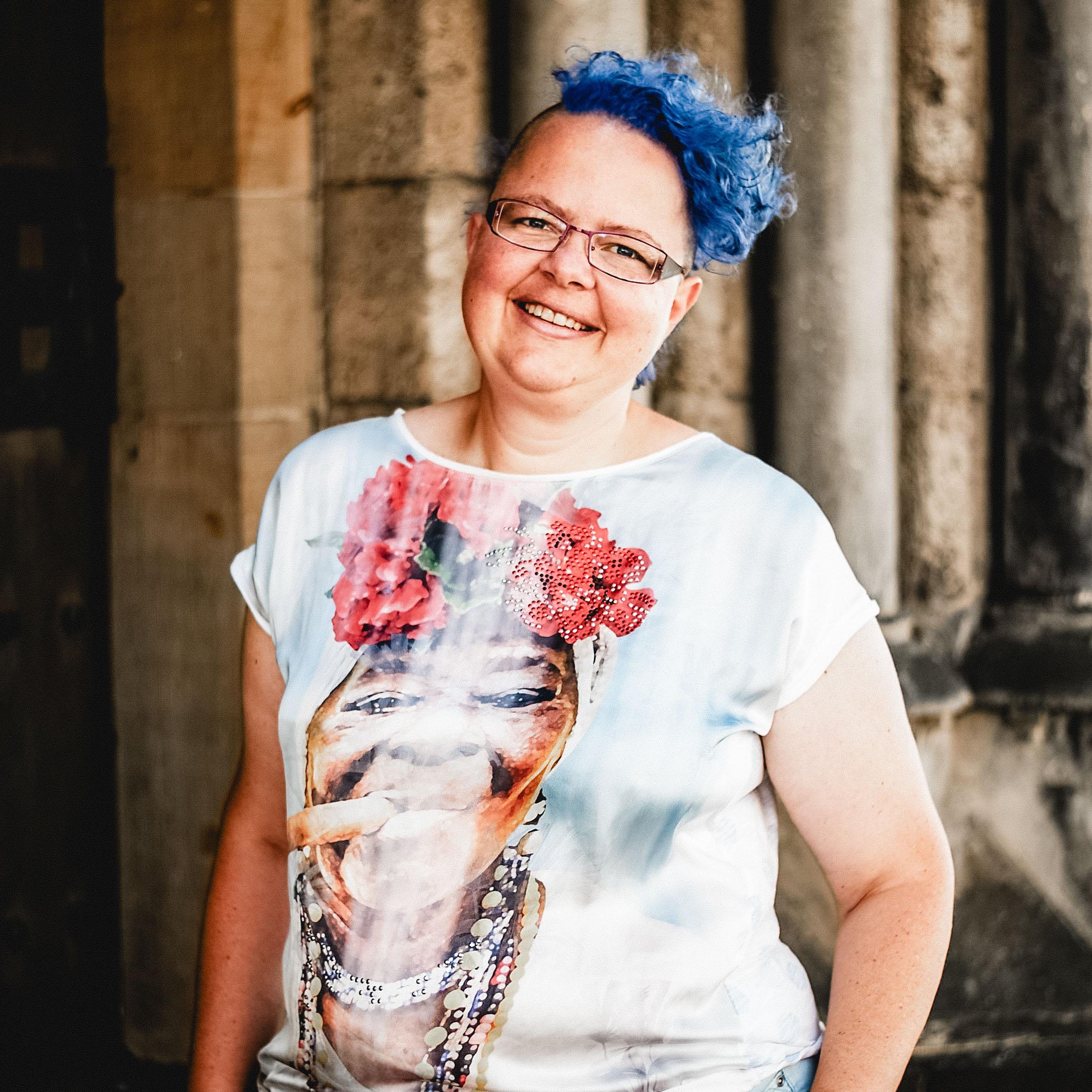 Eine lachende Frau mit blauen Haaren und einem bunten T-Shirt