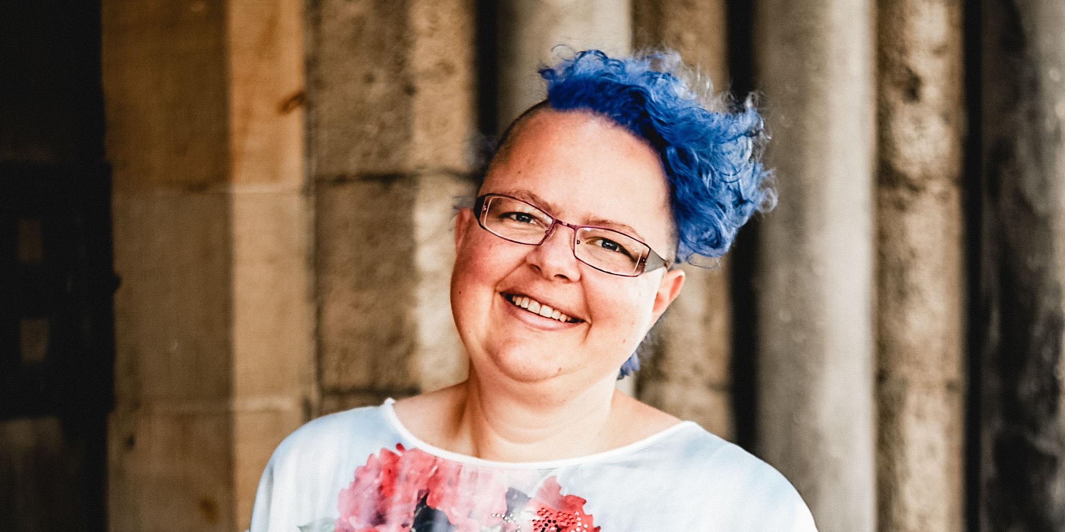 Eine lachende Frau mit blauen Haaren und einem bunten T-Shirt