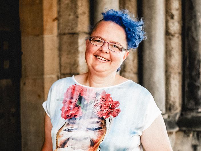 Eine lachende Frau mit blauen Haaren und einem bunten T-Shirt