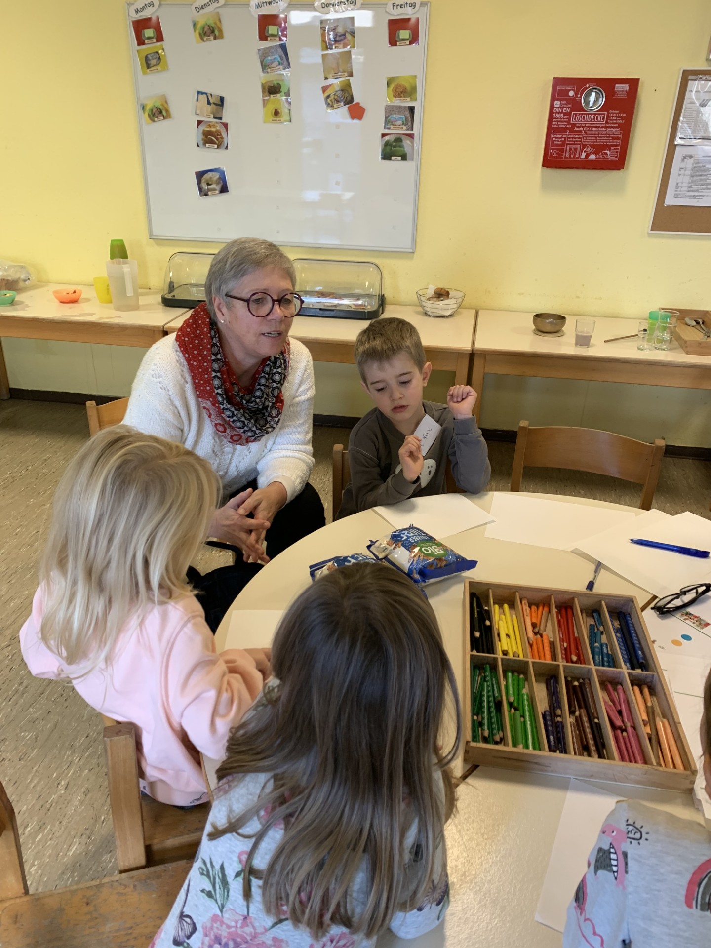 eine Erwachsene sitzt mit drei Kindern an einem Tisch