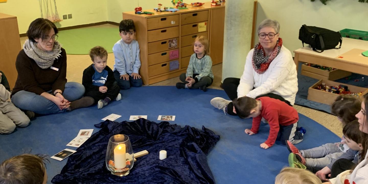 In einem Sitzkreis sitzen mehrere Kinder, zwei Erwachsene sitzen dabei.