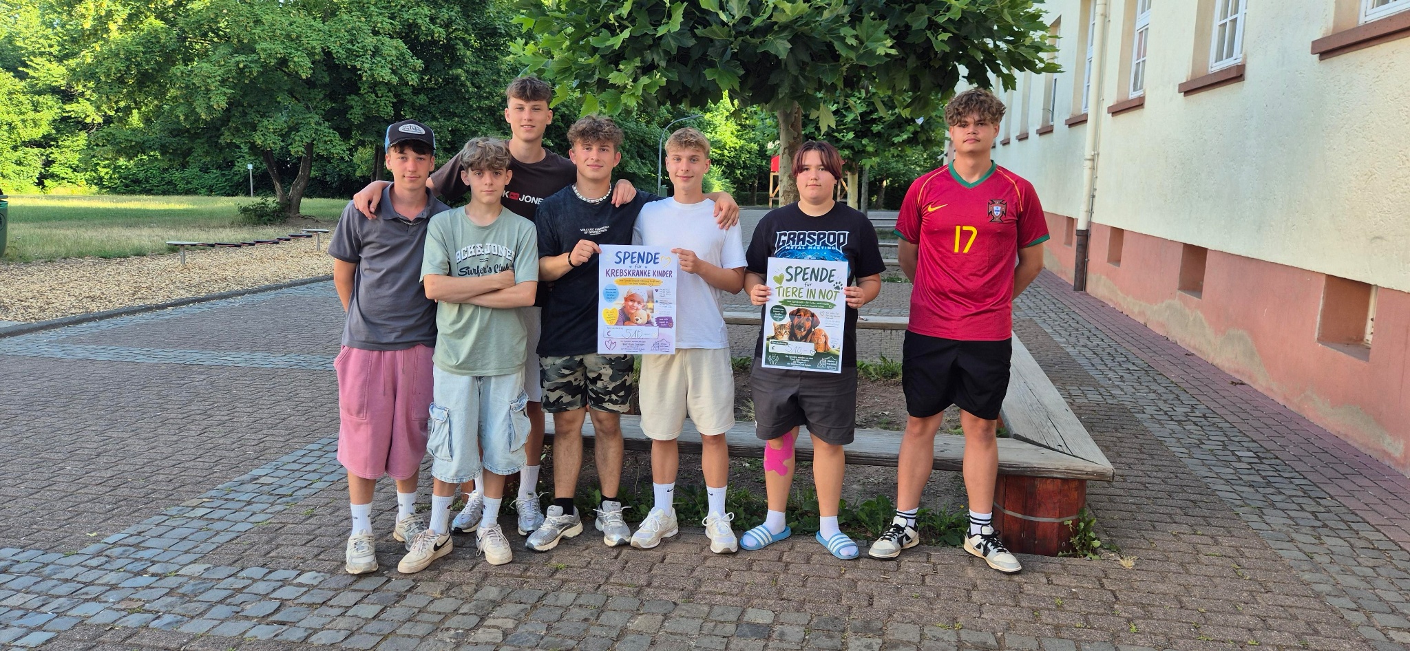 7 Jugendliche vor einem Baum mit einem großen Plakat in den Händen