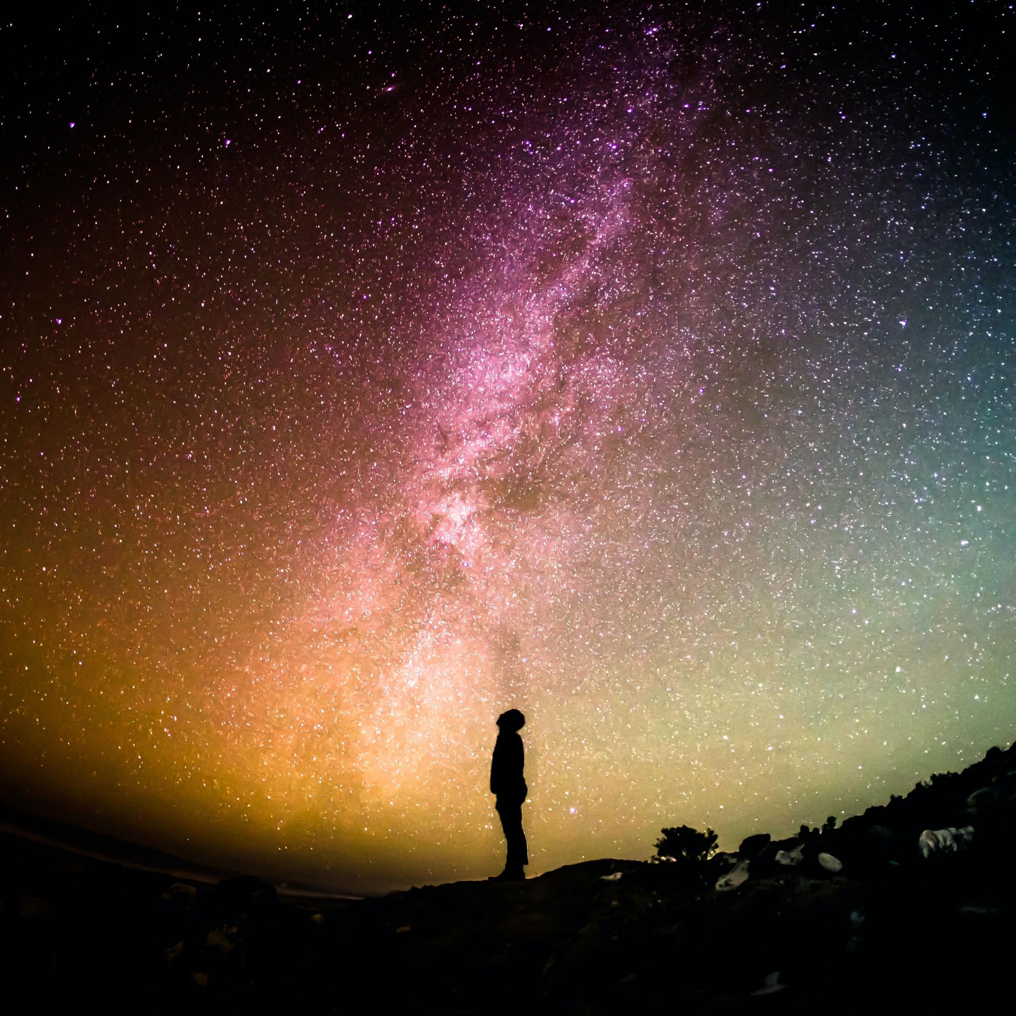 Ein Mensch steht vor einem Sternenhimmel. Man sieht die Milchstraße